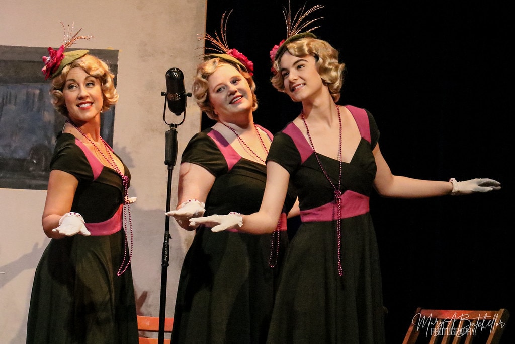 Annie — three women in matching black and pink 1930s dresses perform a trio number