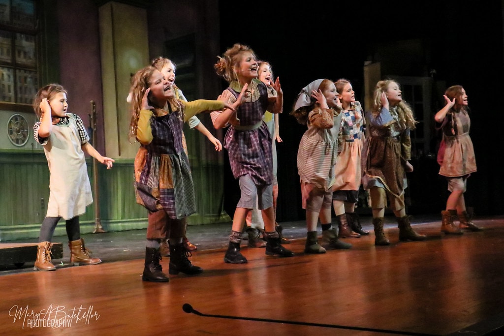 Annie — eight orphan girls stand in a diagonal line singing with hands raised to their cheeks