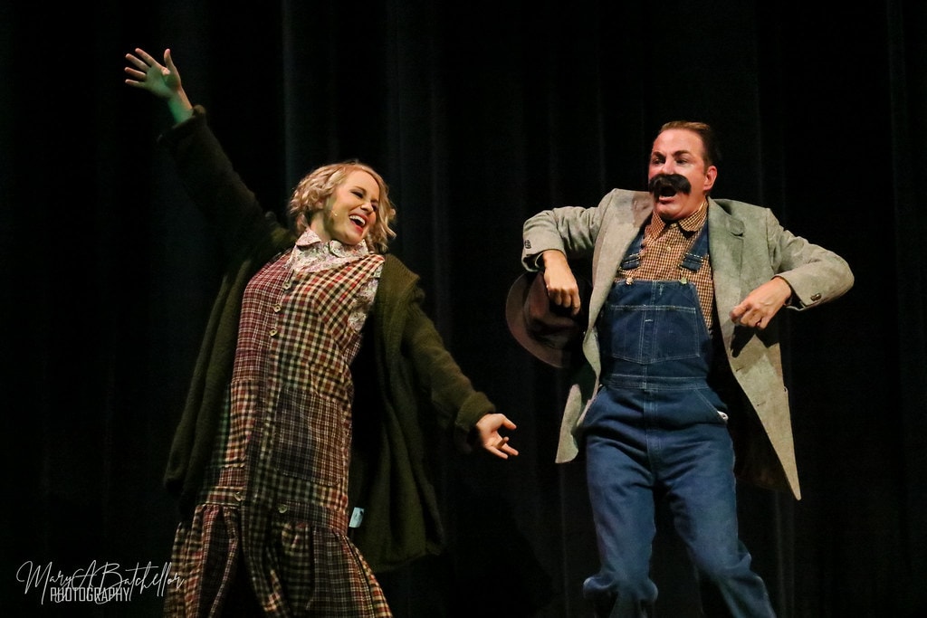 Annie — woman in plaid dress and man in overalls dance joyfully together