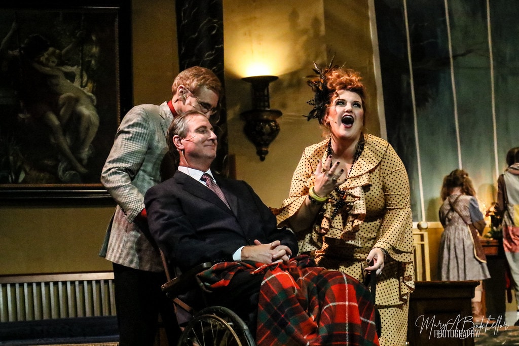 Annie — Rooster leans over a seated Warbucks as Miss Hannigan gestures dramatically