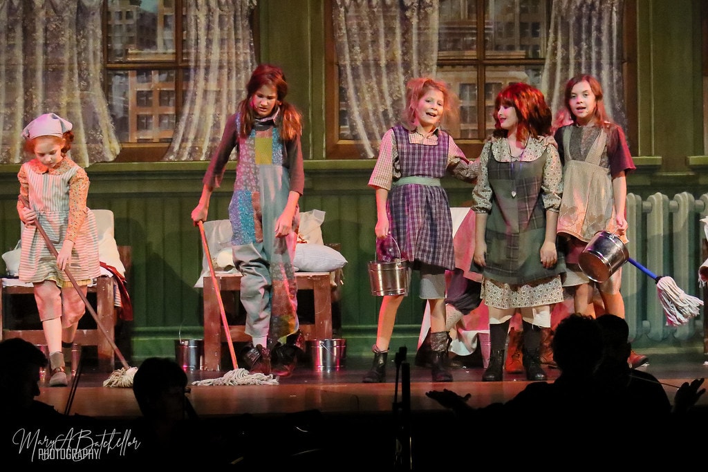 Annie — five orphan girls in ragged patchwork dresses sing and dance with mops and buckets