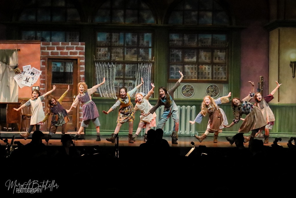 Annie — nine orphan girls leap with arms wide in an exuberant ensemble moment