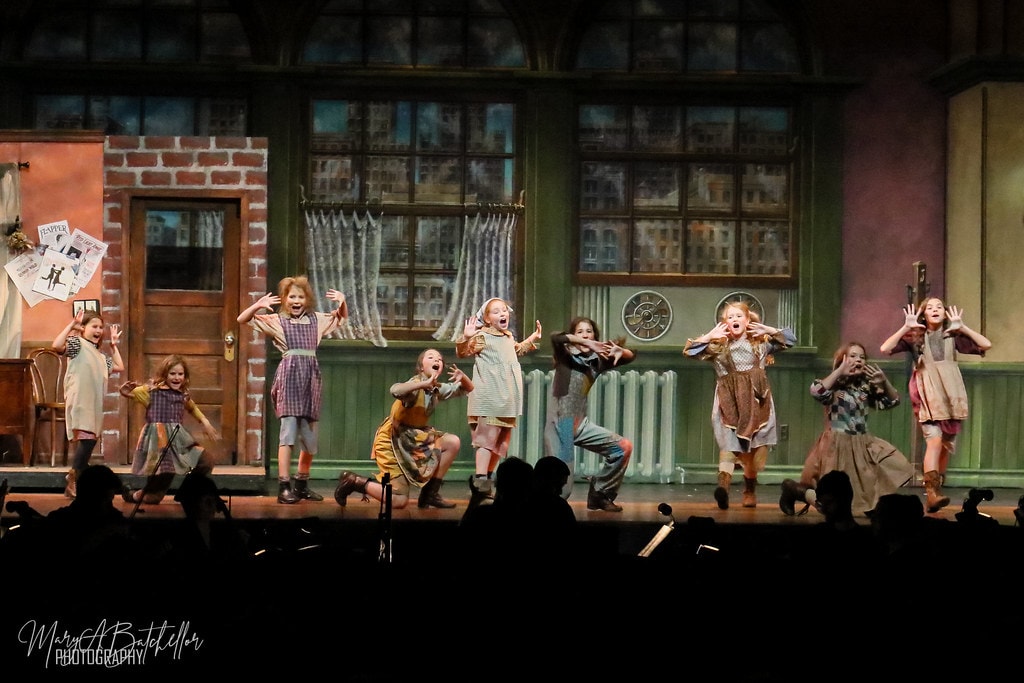 Annie — ten orphan girls react with dramatic open-mouthed expressions in a comedic scare moment