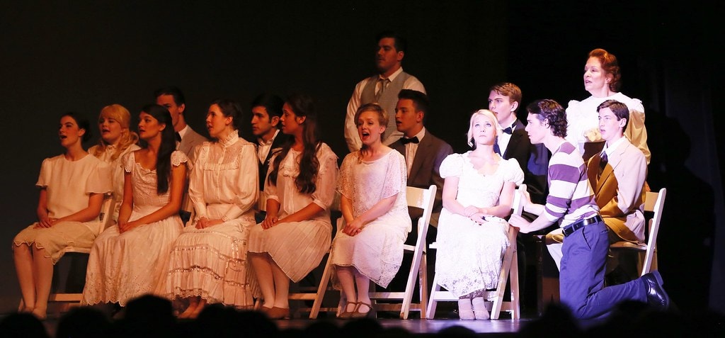 Full ensemble in white dresses singing on chairs — Carousel