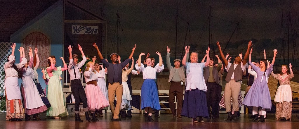 Full Nettie's Spa ensemble with arms raised at harbor — Carousel