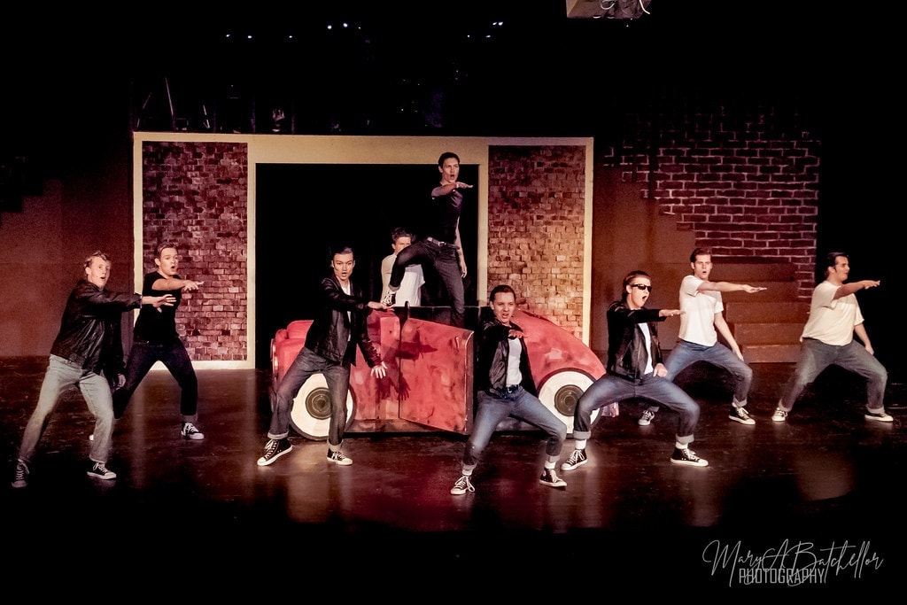 Grease — T-Birds dancing around red car prop with brick backdrop