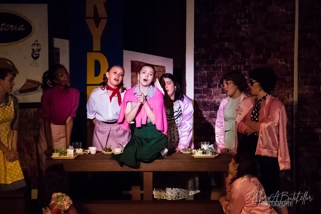 Grease — full cast arms raised finale at Burger Palace set
