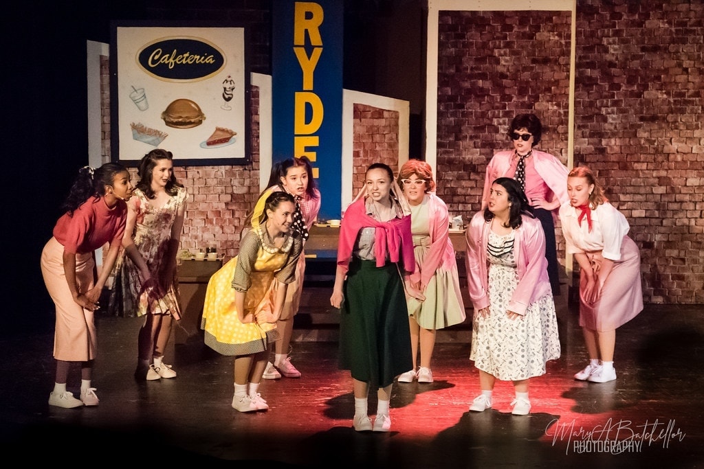 Grease — ensemble cast performing Rydell High number on bare stage
