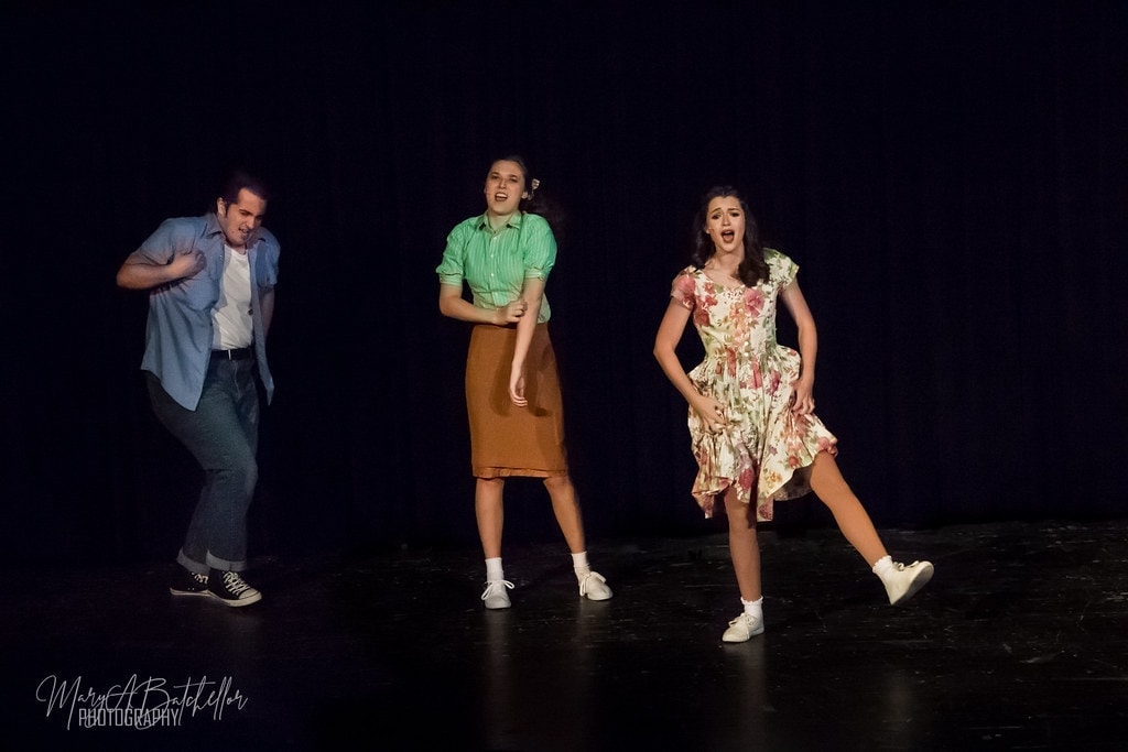 Grease — three performers singing and dancing on dark stage