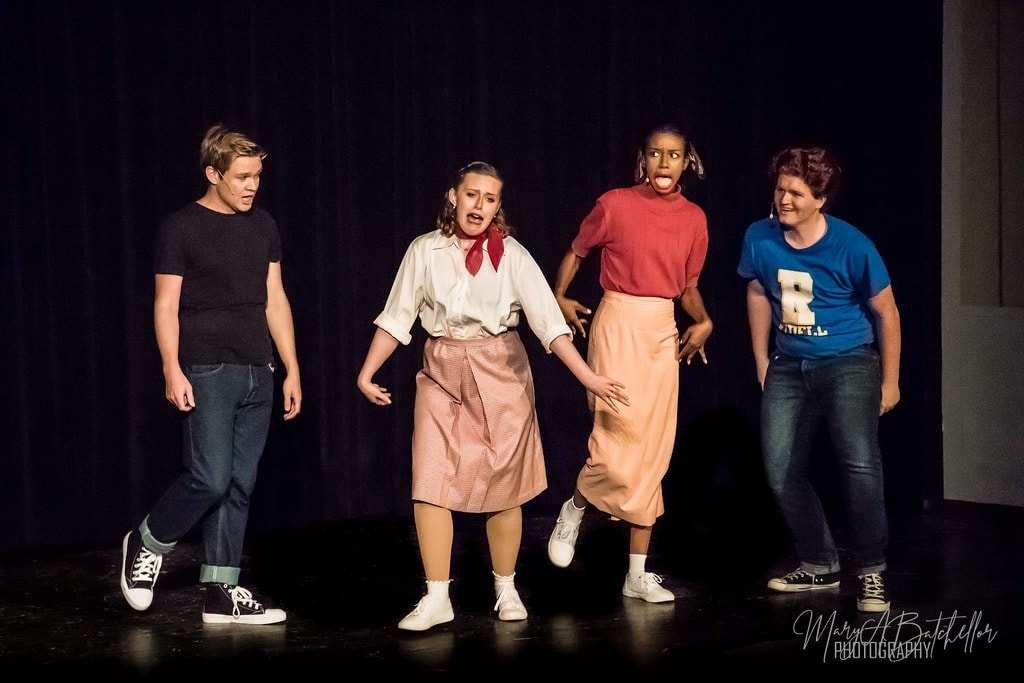 Grease — four performers in comedic scene on dark stage