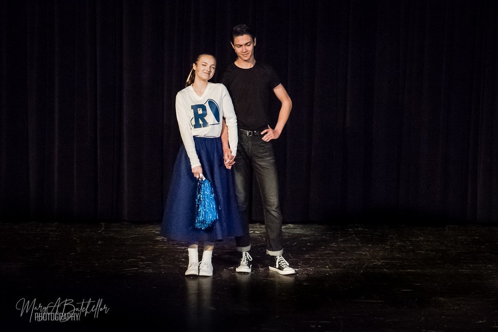 Grease — Sandy in Rydell cheerleader uniform holding hands with Danny