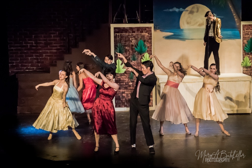 Grease — full cast dancing at the beach party with tropical moon backdrop