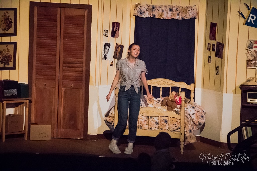 Grease — Sandy in casual jeans and tied shirt singing joyfully