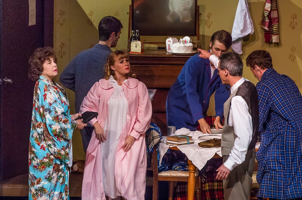 Gypsy — six performers in the boarding house set: Rose in her floral kimono stands at left with a look of concern as Louise in a white nightgown stands center while three men and an older man in a vest crowd around the table with a birthday cake on the dresser behind them