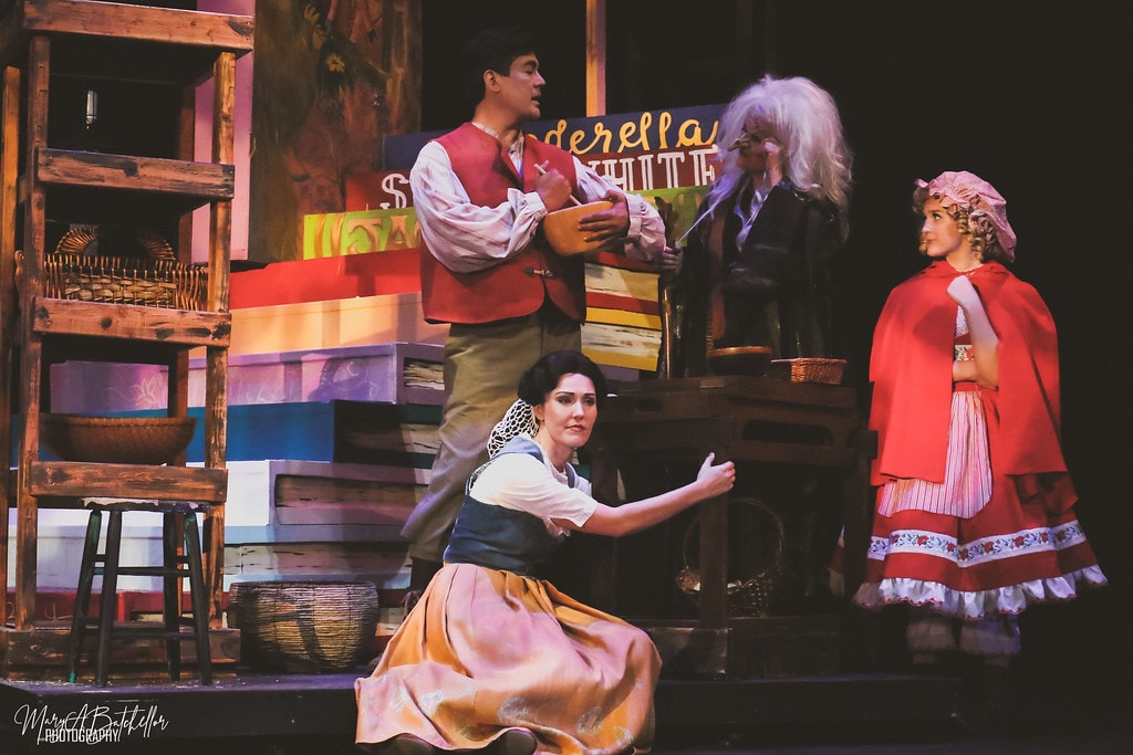 Into the Woods — the Baker's Wife crouches center stage as Jack, the Witch, and Little Red Riding Hood look on before the storybook backdrop