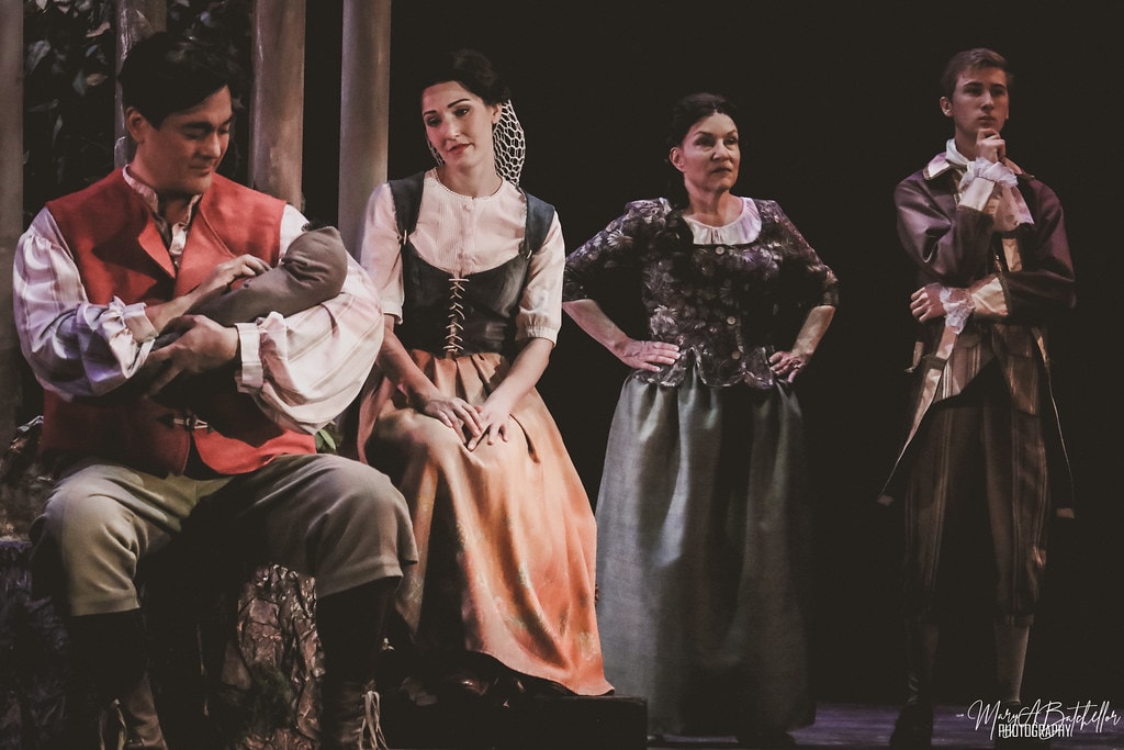 Into the Woods — the Baker holds a baby as the Baker's Wife, the Witch, and Cinderella's Prince look on in the forest set