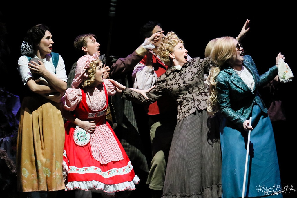 Into the Woods — six cast members react in shock with arms raised in the dark enchanted forest