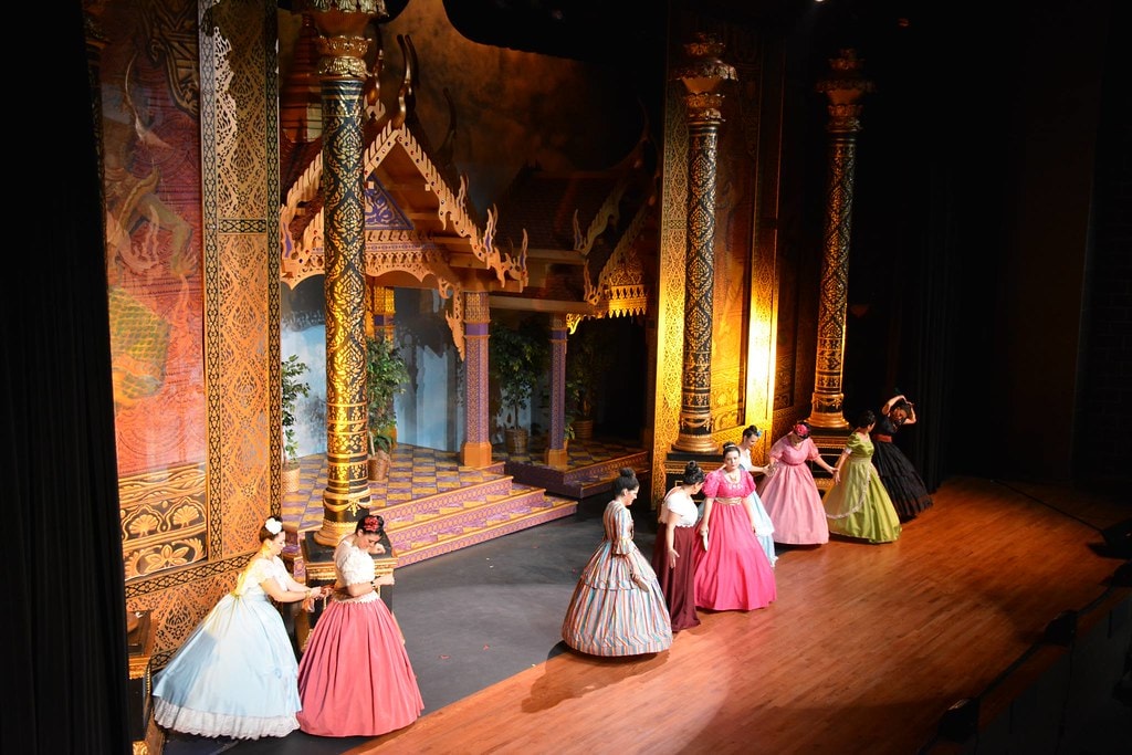 The King & I — performers in Victorian ball gowns dancing before the ornate temple columns in the golden-lit palace set