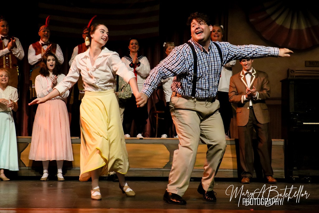 The Music Man — a young woman in a yellow skirt and a man in a plaid shirt dance joyfully