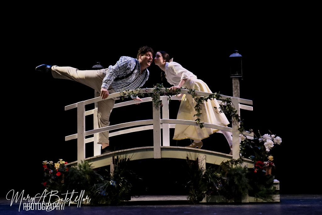 The Music Man — a couple leans in for a kiss on the white garden bridge