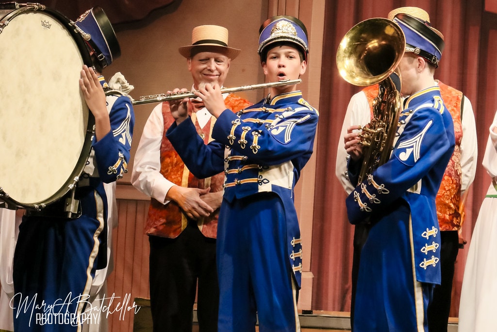 The Music Man — Harold Hill watches as a boy in a blue marching band uniform plays the flute