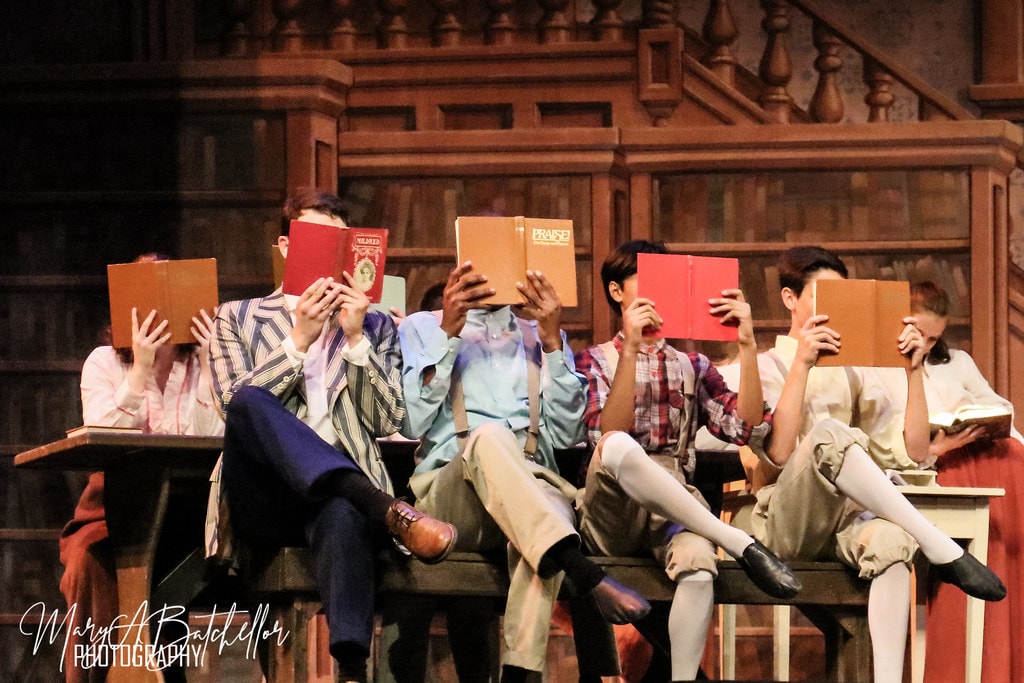 The Music Man — six students in period costumes hold books open in the library classroom scene