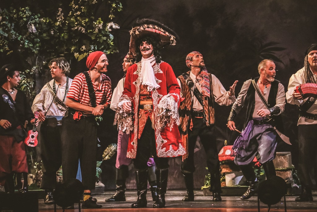 Peter Pan — Captain Hook in his red coat and tricorn hat stands center stage with his scallawags in the jungle