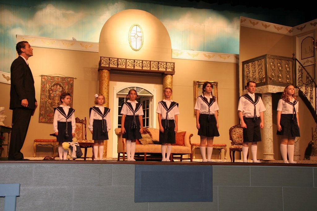 The Sound of Music — Captain von Trapp in a black suit stands at left as the seven children in matching navy sailor uniforms line up at attention in the grand von Trapp villa interior set