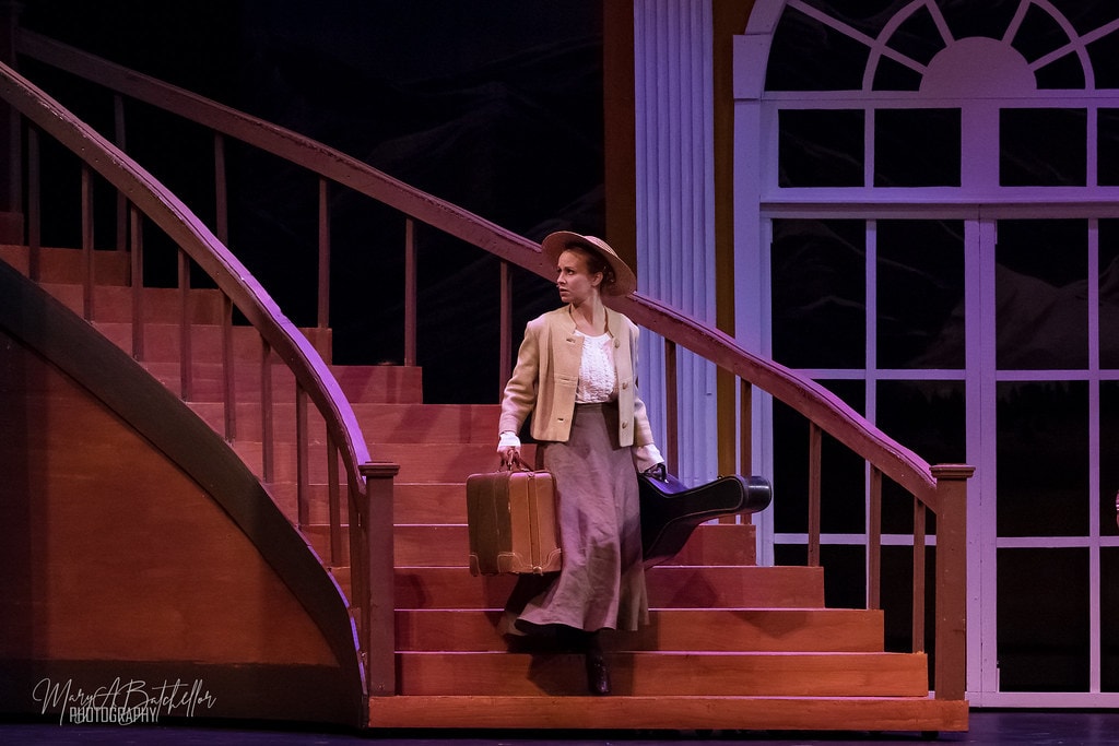 The Sound of Music — Maria in tan jacket carrying two suitcases down the staircase