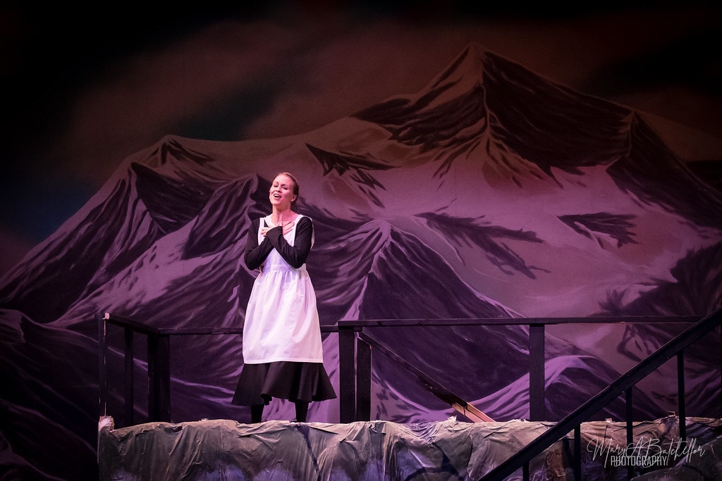 The Sound of Music — Maria in white apron singing before purple-lit Alpine backdrop