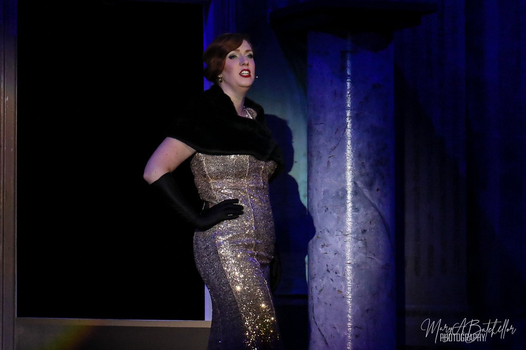 Thoroughly Modern Millie — a woman in a gold sequined gown and black fur stole sings a dramatic solo