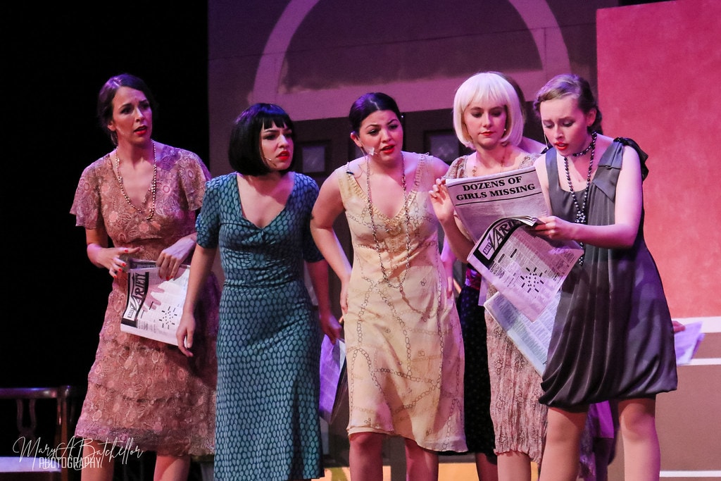 Thoroughly Modern Millie — five women in 1920s beaded dresses read a Variety newspaper headline