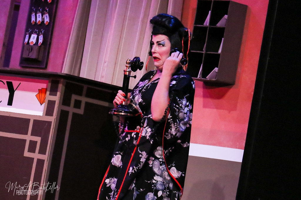 Thoroughly Modern Millie — Mrs. Meers in a black floral kimono holds a vintage candlestick telephone at the hotel front desk