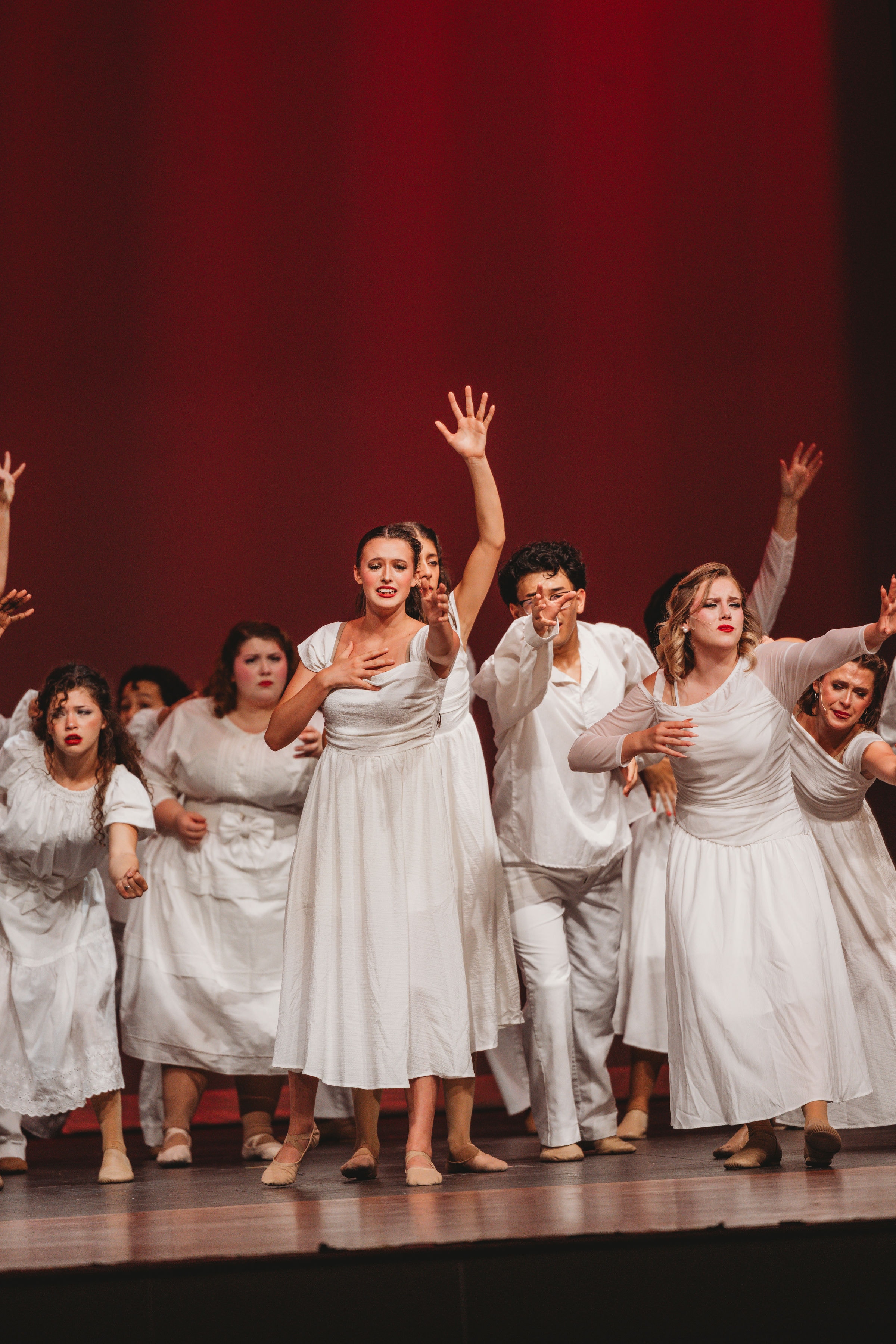 West Side Story 2026 - ensemble cast performing with raised arms on red backdrop